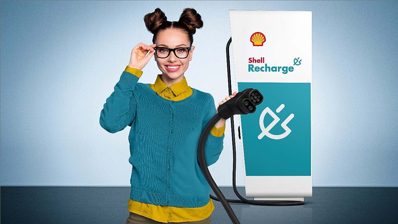 Junge Frau hält lächelnd den Ladestecker einer Shell Recharge Ultraschnellladesäule in der Hand.