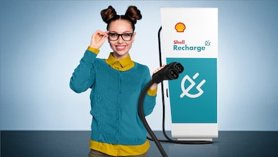 Junge Frau hält lächelnd den Ladestecker einer Shell Recharge Ultraschnellladesäule in der Hand.
