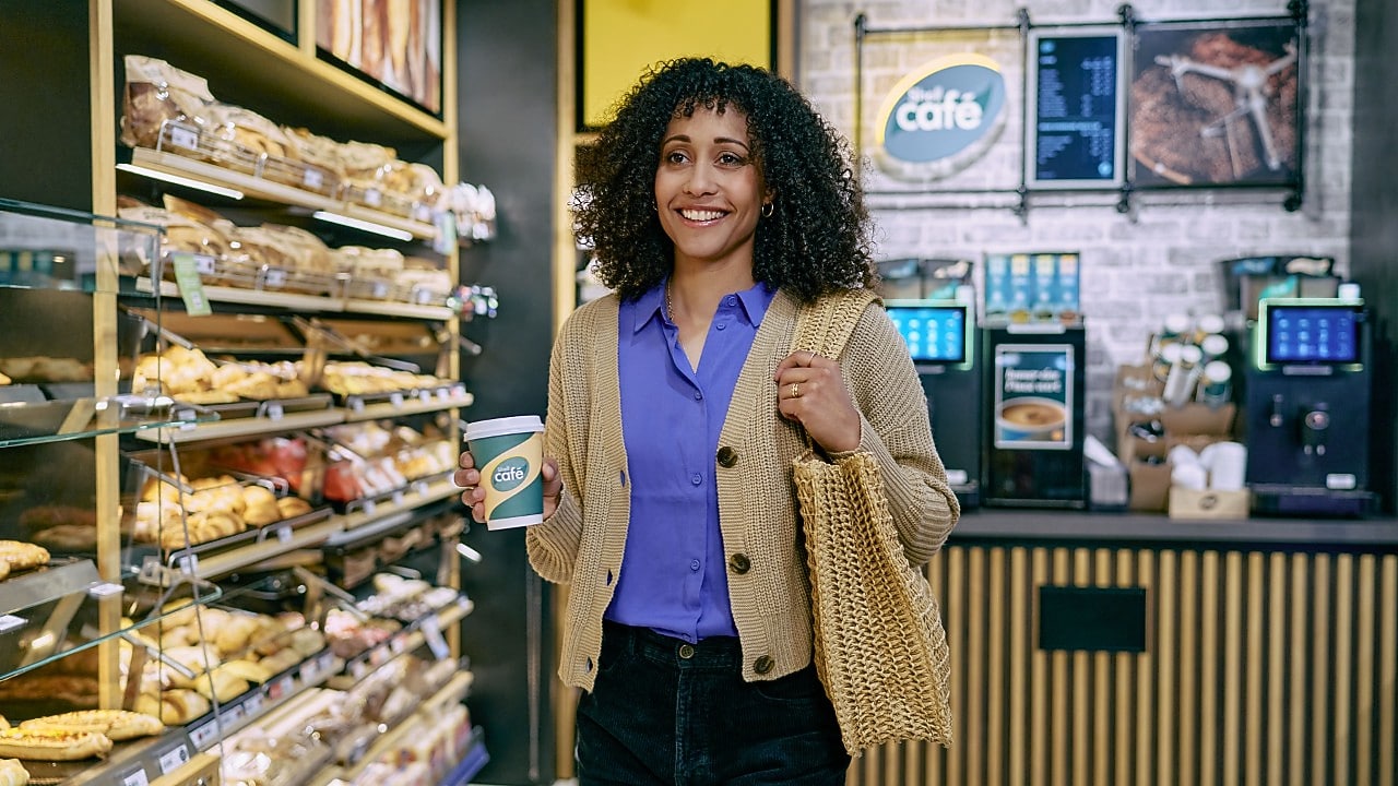 Eine Frau, im Shell Shop und einem Shell Café Heißgetränk in der Hand