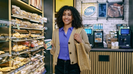 Eine Frau, im Shell Shop und einem Shell Café Heißgetränk in der Hand