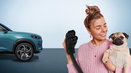 Frau hält einen Hund und einen EV-Ladestecker; daneben steht ein blaues 