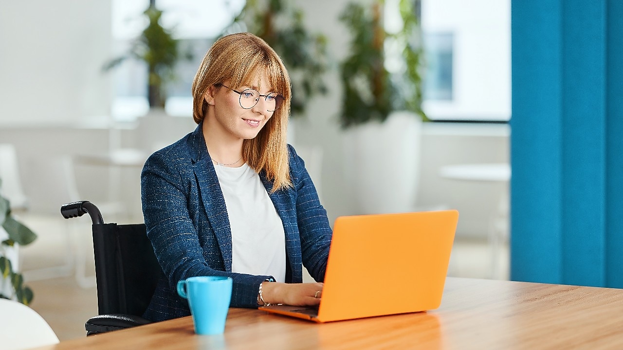 Eine Person im Rollstuhl, die in einem Büro an einem Laptop arbeitet
