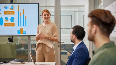 Eine Person präsentiert vor einem großen Bildschirm mit farbigen Diagrammen