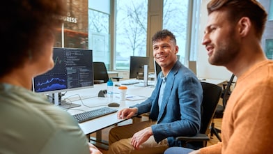Team sitzt am Schreibtisch und betrachtet Daten auf Monitoren in einem Büro