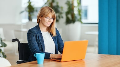 Eine Person im Rollstuhl, die in einem Büro an einem Laptop arbeitet