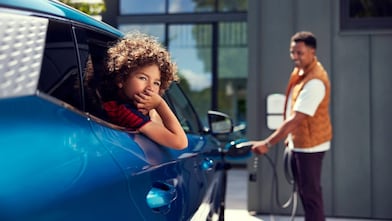 Ein Vater lädt ein Elektrofahrzeug auf, während sein Sohn darin wartet