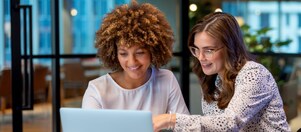Two women working together in front of a computer and discussing