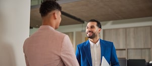Zwei Personen in Geschäftskleidung geben sich in einem modernen Büro die Hand