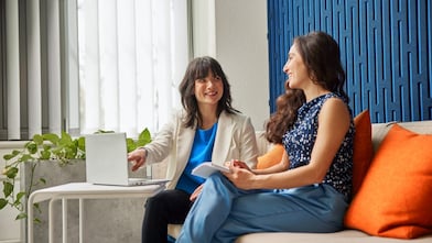 Personen sitzen auf einem Sofa und besprechen etwas an einem Laptop