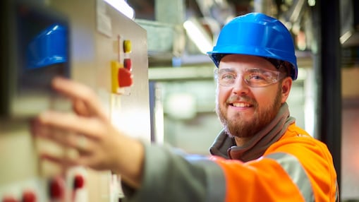 Arbeiter bedient eine industrielle Schalttafel mit Schutzhelm und Warnkleidung