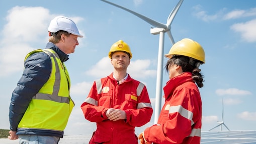 Drei Fachkräfte in Sicherheitskleidung stehen draußen bei Windkraftanlagen und diskutieren.