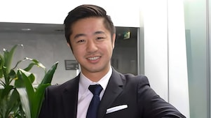 Ein lächelnder Mann im Blazer und mit Krawatte steht in einem modernen Büro mit Pflanzen im Hintergrund