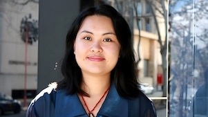 Eine Person im blauen Hemd lächelt sanft mit einer unscharfen urbanen Szene im Hintergrund