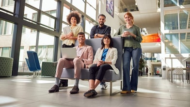 Gruppe steht und sitzt gemeinsam in einer offenen, modernen Gebäudelobby