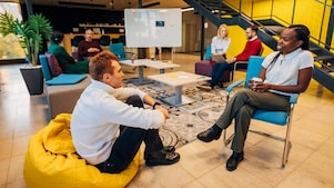 Eine Person im weißen Pullover sitzt auf einem gelben Sitzsack einer anderen Person gegenüber