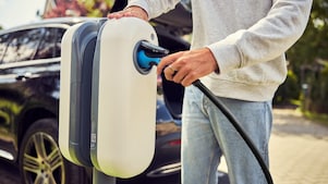 Eine Person schließt ein Ladegerät für Elektrofahrzeuge an eine Ladestation im Freien an.