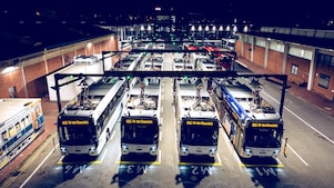 Draufsicht auf Elektrobusse, die nachts auf einem Betriebshof geparkt und an Ladegeräte angeschlossen sind.