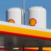 Zwei weiße Kraftstofftanks mit Shell-Logos stehen hinter einem Vordach einer Shell-Tankstelle.