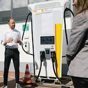 Ein Mann erklärt einer Frau eine Shell Recharge Ladestation.