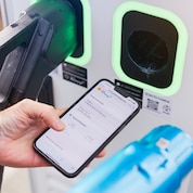 Eine Person hält ein Smartphone mit der Shell Recharge App vor einer Ladestation.
