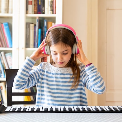 Ein junges Mädchen, konzentriert und mit rosa Kopfhörern, spielt auf einem Klavier.