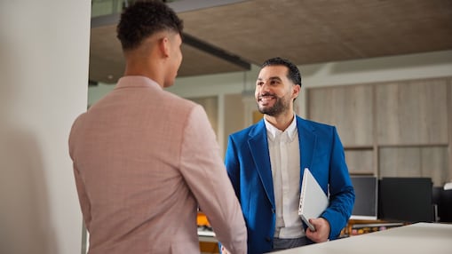 Zwei Personen in Geschäftskleidung geben sich in einem modernen Büro die Hand