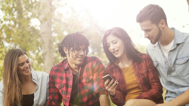 Junge Leute im Park, die zusammen auf ein Telefon schauen