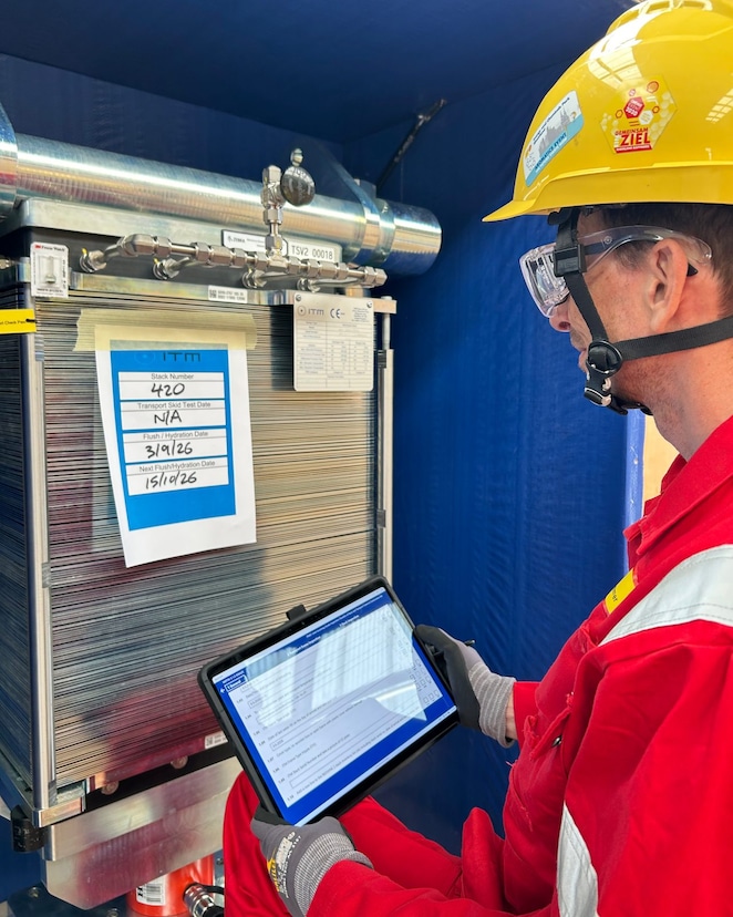 Worker conducts a digital inspection of an electrolyser stack using a tablet in an industrial environment.