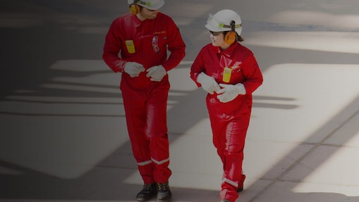 Arbeiter und Arbeiterin in rotem Schutzanzug mit weißem Helm und Gehörschutz