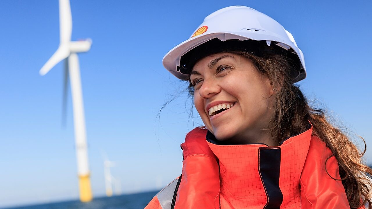Lächelnde Frau mit einem Helm vor einem Offshore-Windrad