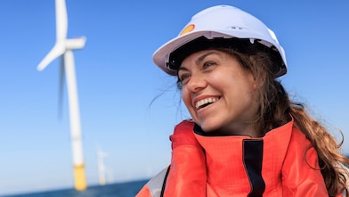 Lächelnde Frau mit einem Helm vor einem Offshore-Windrad
