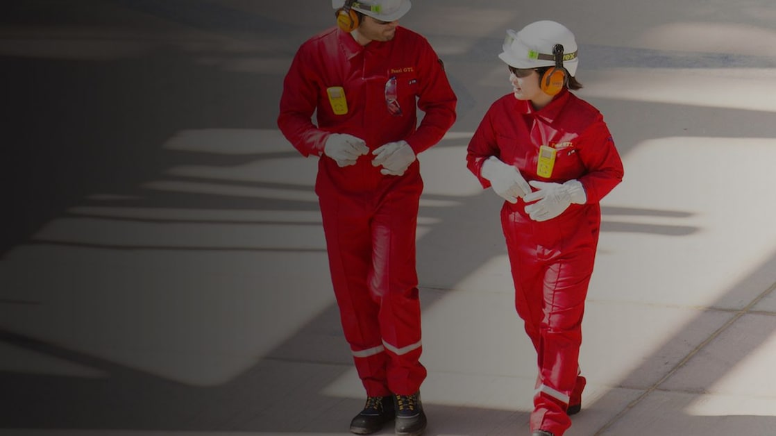 Arbeiter und Arbeiterin in rotem Schutzanzug mit weißem Helm und Gehörschutz