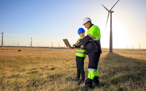 2 Ingenieure stehen in einem Windpark mit einem Laptop.