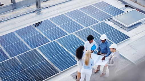 Eine Gruppe von Menschen steht auf einem Dach neben Solar Panels