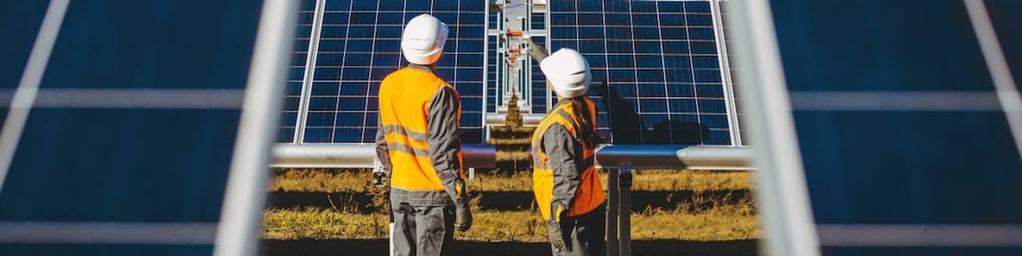 Zwei Arbeiter stehen in einem Feld mit Photovoltaik Anlagen.