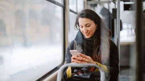 Eine Frau sitzt mit einem Smartphone im Bus