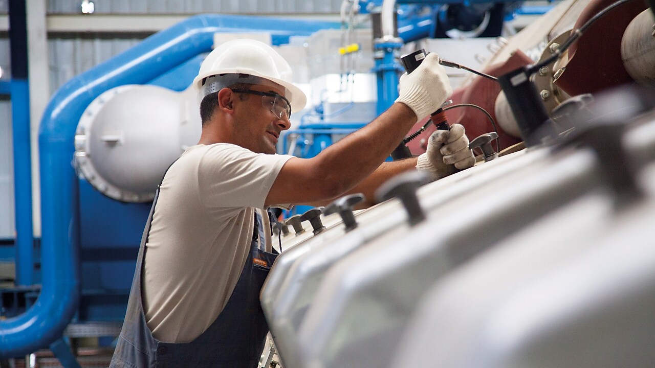 Techniker führt Wartungsarbeiten an einem stationären Gasmotor in einer industriellen Stromerzeugungsanlage durch.