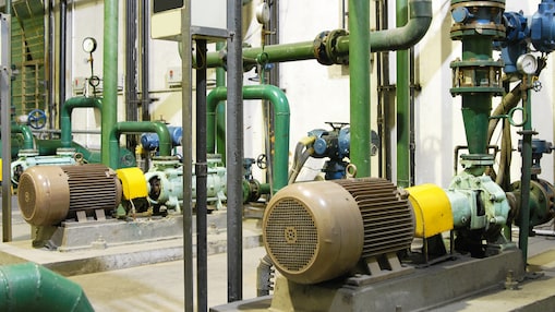 Industrieller Maschinenraum mit Pumpen, Motoren und grünen Rohrleitungen zur Stromerzeugung.