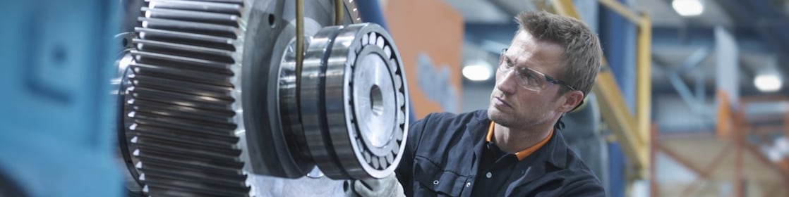 Industrielle Wartung eines großen Zahnradgetriebes in einer Produktionshalle, präzise Schmierung und Maschinenpflege.