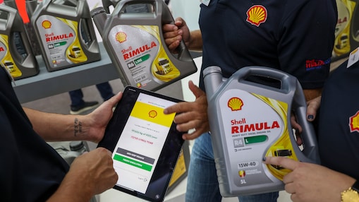 Drei Personen halten Shell Rimula-Flaschen und ein Tablet, auf dem der Shell CO₂-   und Energie-Tracker angezeigt wird. Im Hintergrund sind Regale mit weiteren Shell Rimula-Flaschen zu sehen.