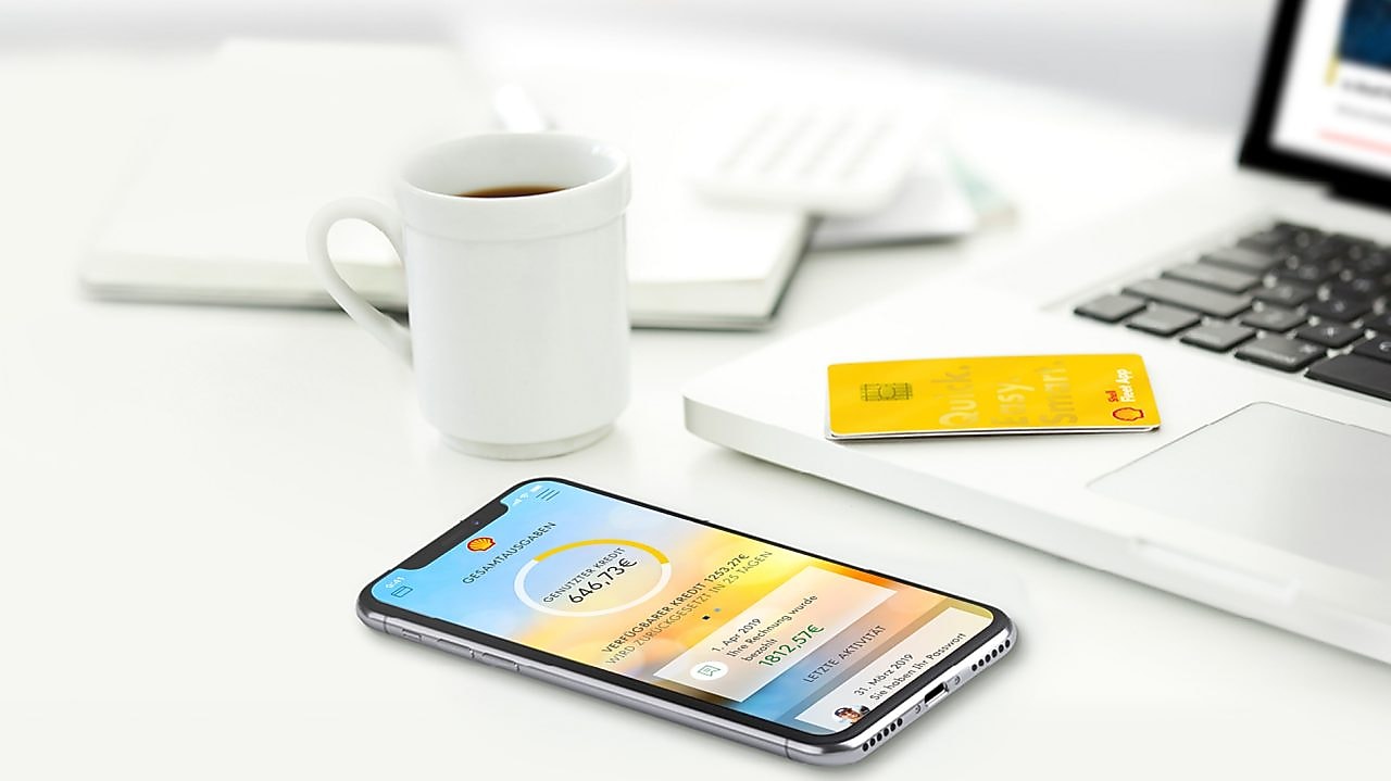 on an office table are a laptop a shell card and a smartphone with the shell fleet app open