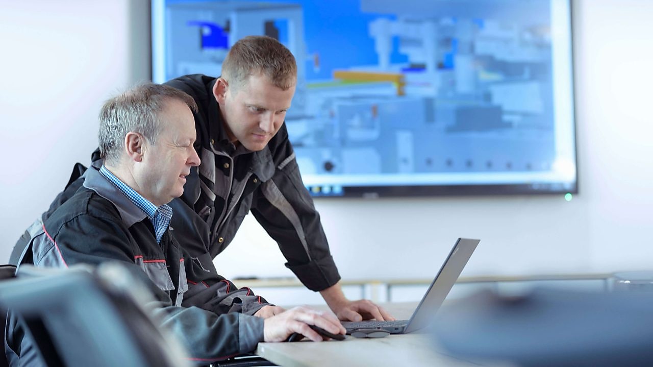 Zwei Techniker sitzen vor einem Laptop und betrachten den Bildschirm.