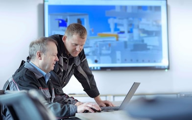 Zwei Techniker sitzen vor einem Laptop und betrachten den Bildschirm.