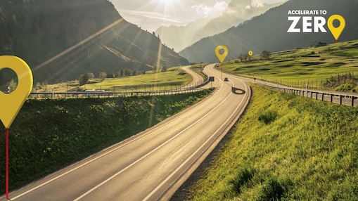 Auto fährt auf einer Schnellstraße durch grüne Landschaft mit Bergen im Hintergrund, Textaufschrift: "Accelerate to Zero".