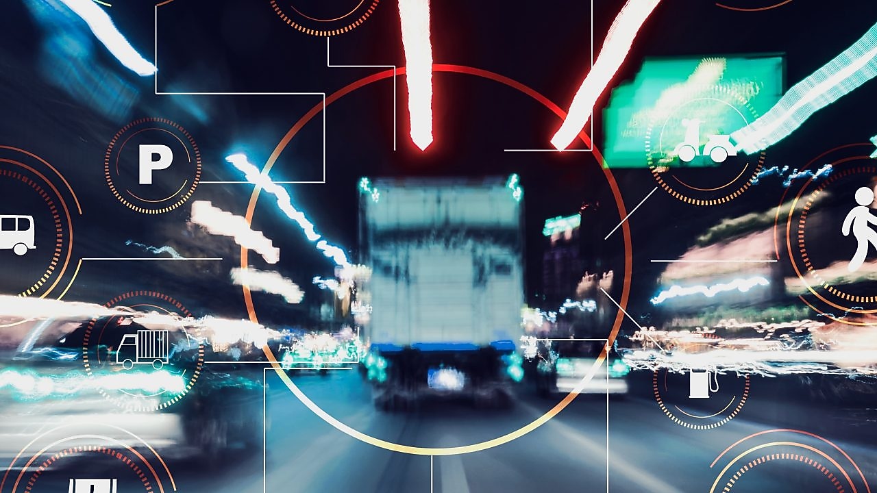 Das Bild zeigt eine Langzeitbelichtung einer belebten Straße bei Nacht, auf der die Lichtspuren vorbeifahrender Fahrzeuge zu sehen sind. Über das Foto sind verschiedene grafische Symbole und Icons gelegt, die sich auf Transport und Mobilität beziehen