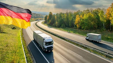 LKWs fahren auf einer Autobahn. Es ist eine Detschland-Flagge zu sehen.
