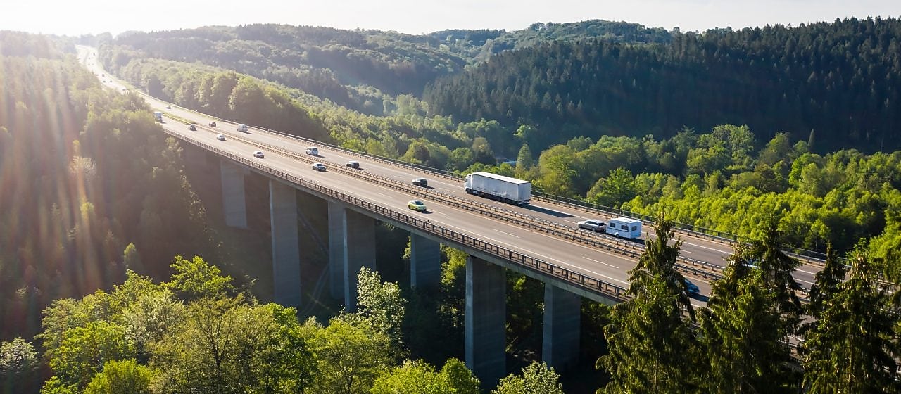 Fahrzeuge fahren auf einer Autobahn-Brücke im Grünen.