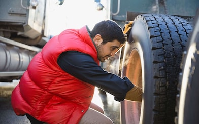 Ein Lkw-Fahrer prüft den Reifen seines Lkw.