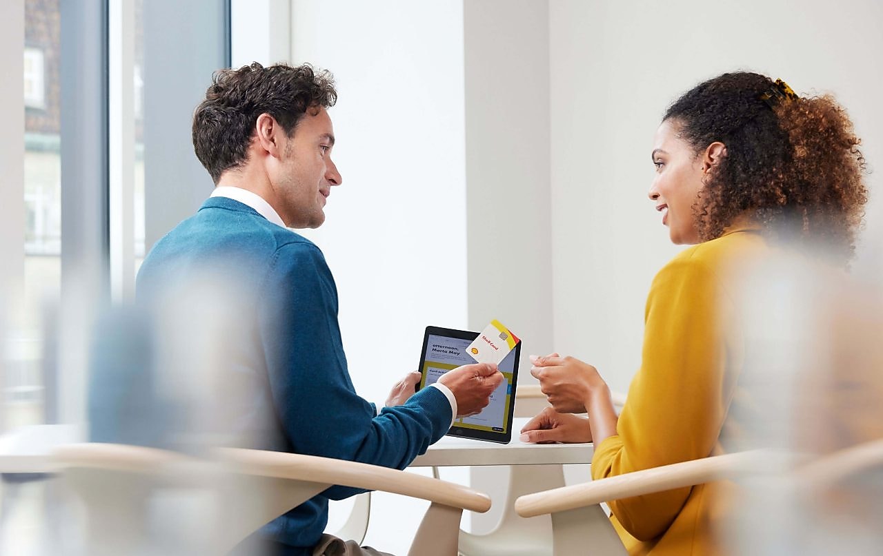 Ein junger Mann übergibt in einem Büro eine Shell Card an eine junge Frau.