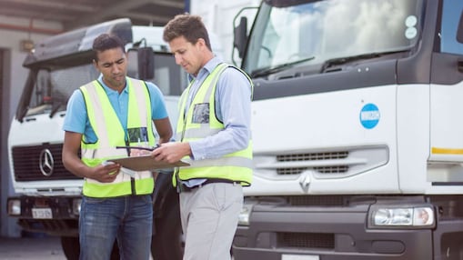 Zwei Fuhrpark-Mitarbeiter blicken vor einem Lkw auf ein Tablet.
